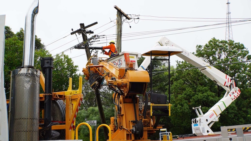 A workman in high vis uses a cherry picker to repair powerlines in a suburban street