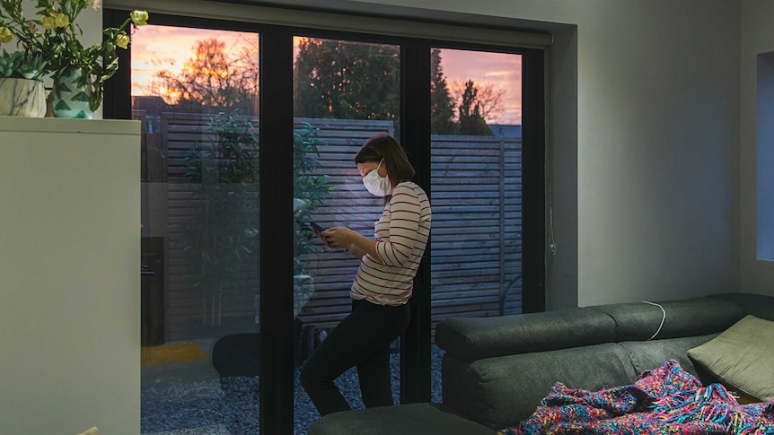 Woman in self isolation using smartphone by window.
