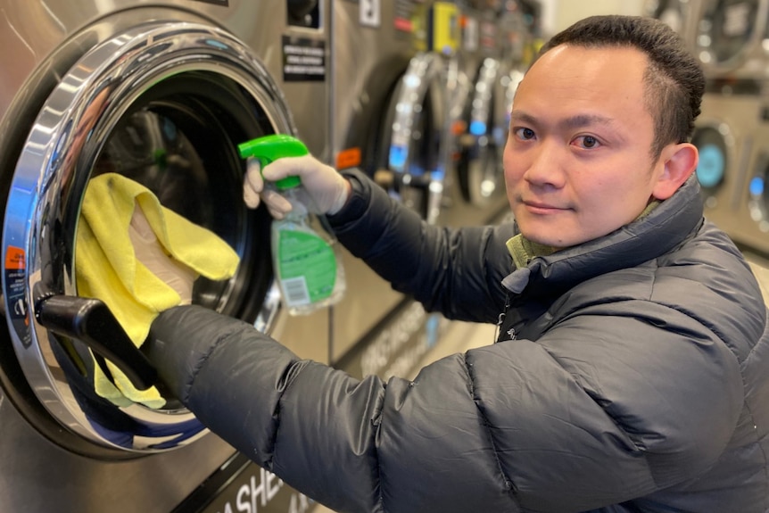 Hung Vo cleans the outside of a silver washing machine in a laundromat.