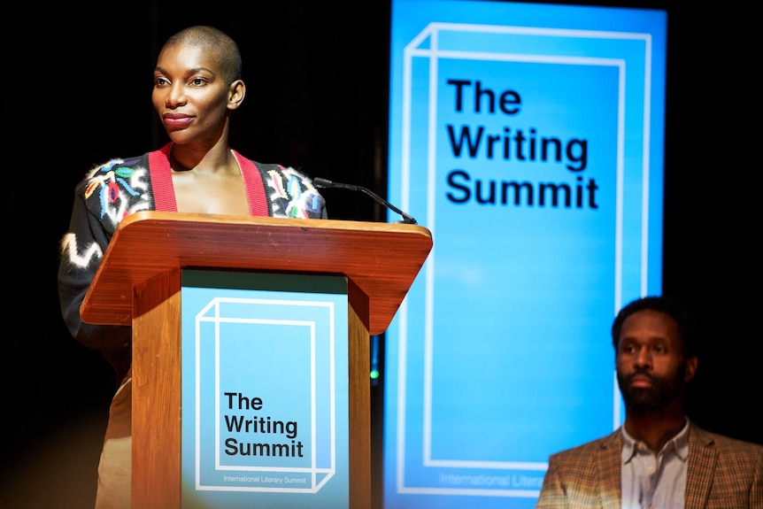 A scene from the TV series I May Destroy You with Michaela Coel, speaking on stage at a writing summit