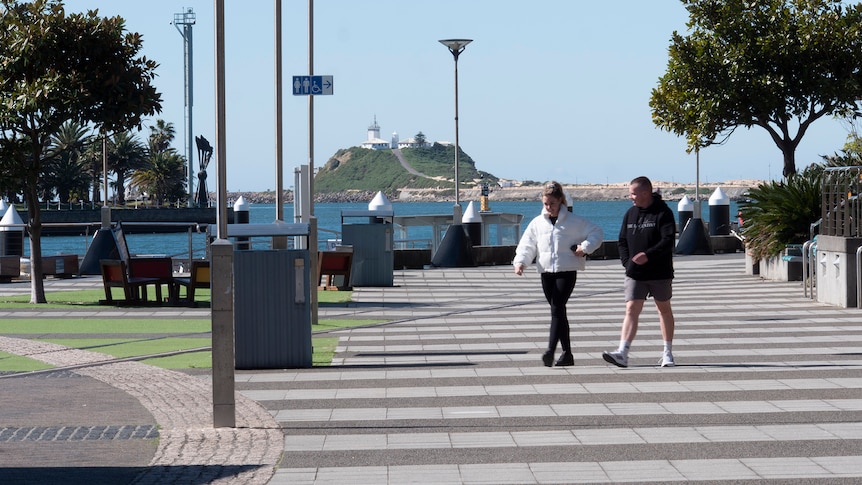 Two people walking along promenade in Newcastle with the ocean in the background