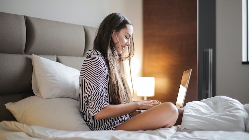 A woman in a striped shirt uses a laptop on her bed