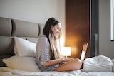 A woman in a striped shirt uses a laptop on her bed