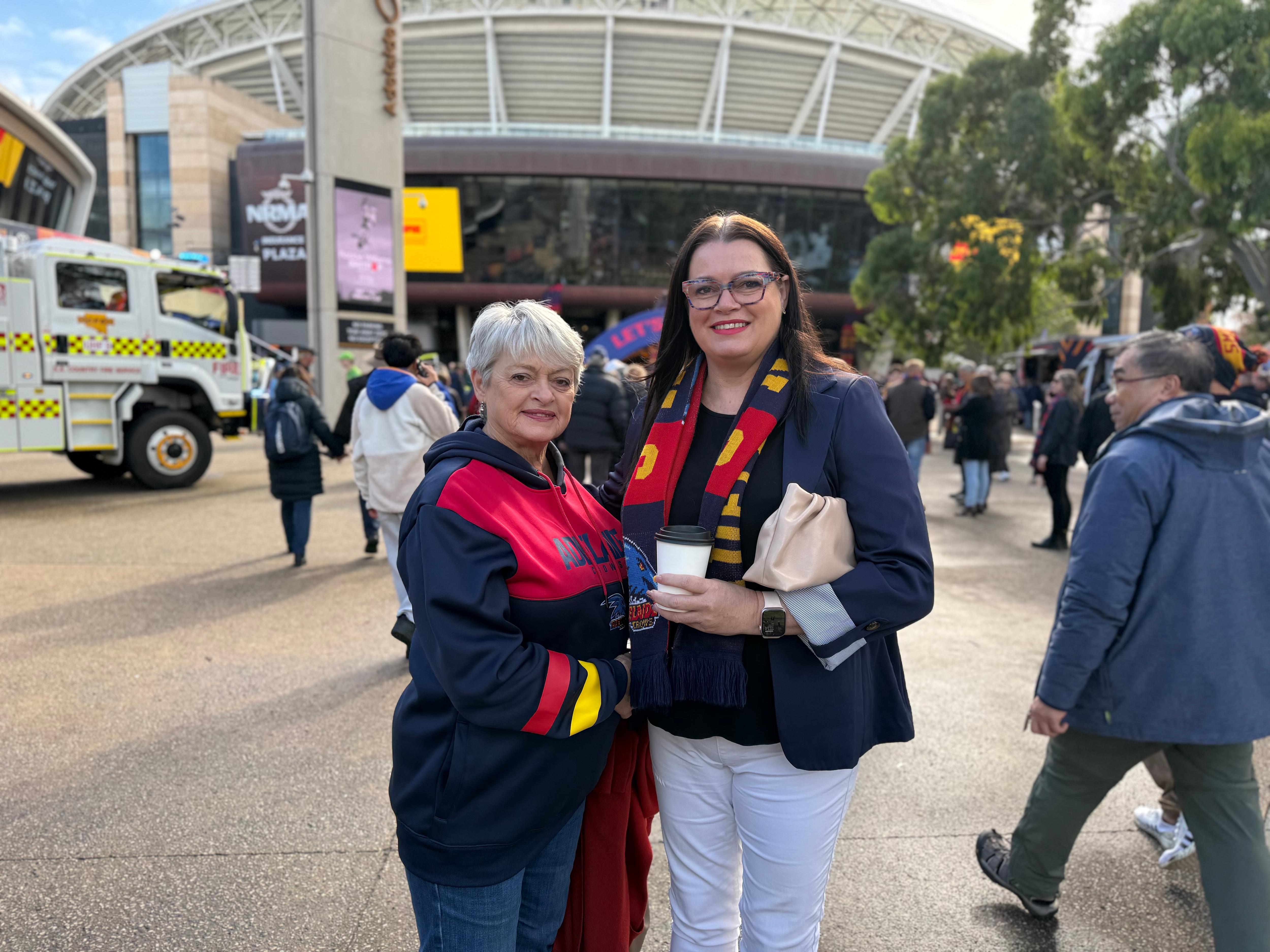 Two women wearing Crows fan gear in a forecourt