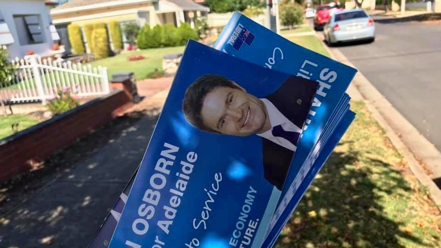 A hand holding a bunch of blue flyers with Liberal candidate Shaun Osborn's face on them