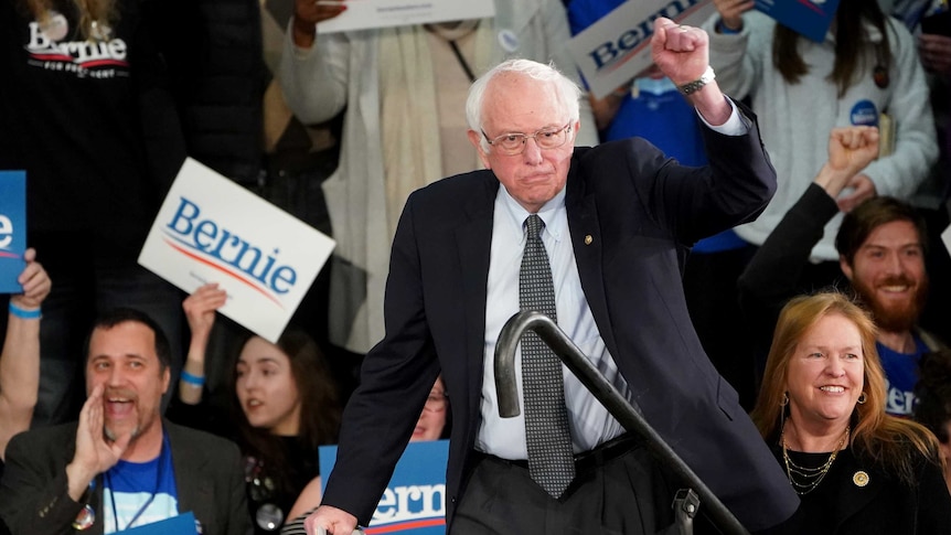 Bernie Sanders hold up his fist before crowds holding 'Bernie' signs