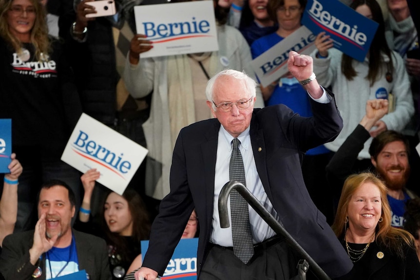 Bernie Sanders hold up his fist before crowds holding 'Bernie' signs