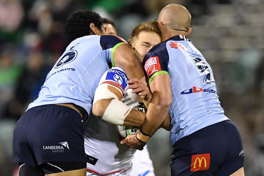 A St George Illawarra NRL player makes a hit-up as he is tackled by two Canberra opponents.