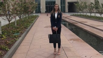 A woman stands in front of Parliament House smiling