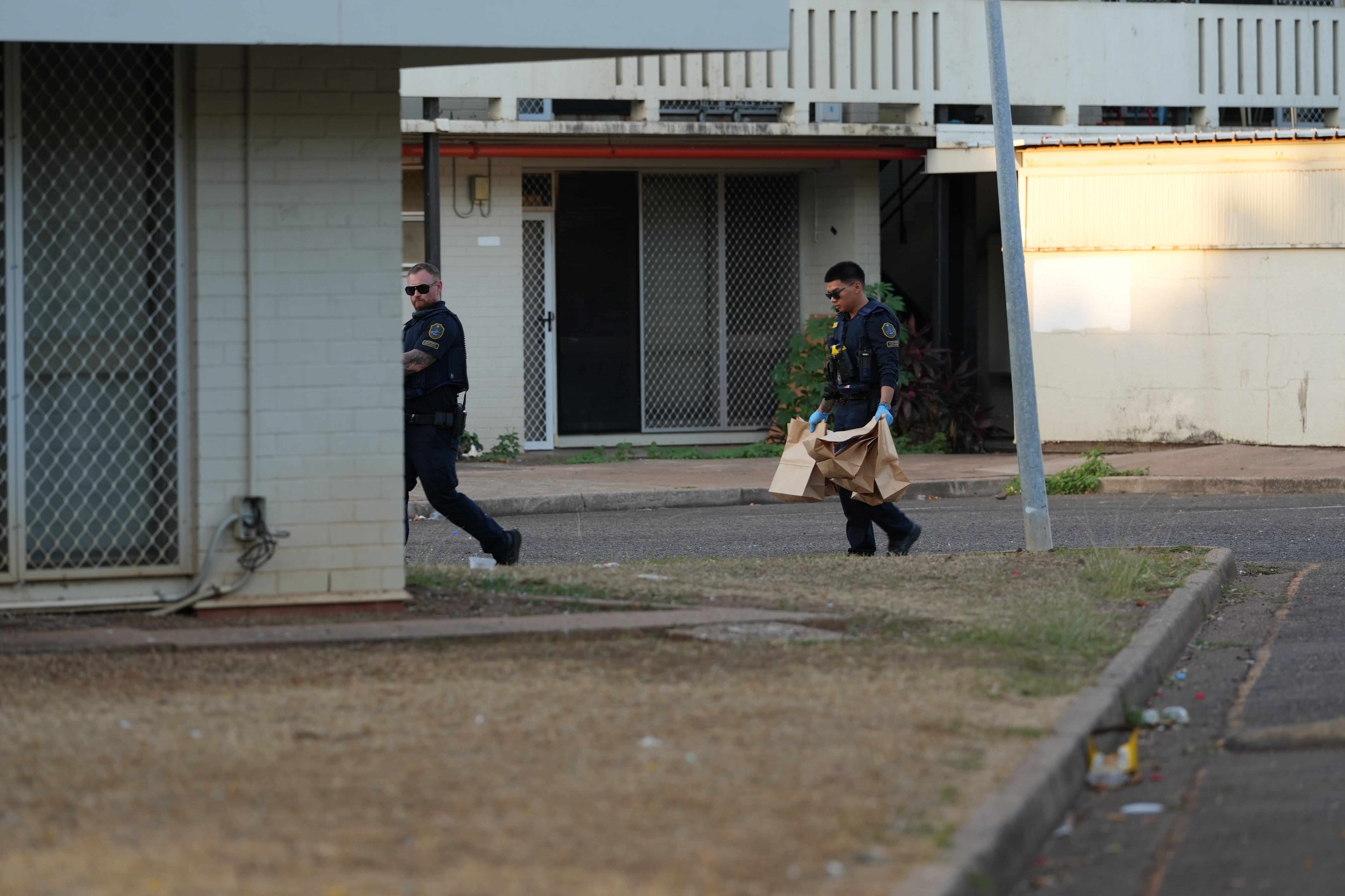 Two men in police uniforms walk through the outside of a building complex holding brown bags