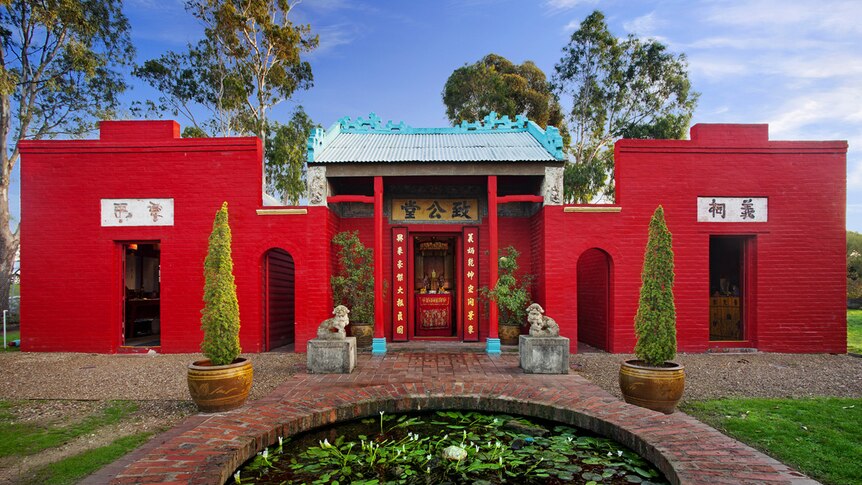 From a low angle, you look across a red brick water feature that shows Bendigo's bright read Joss House Temple.