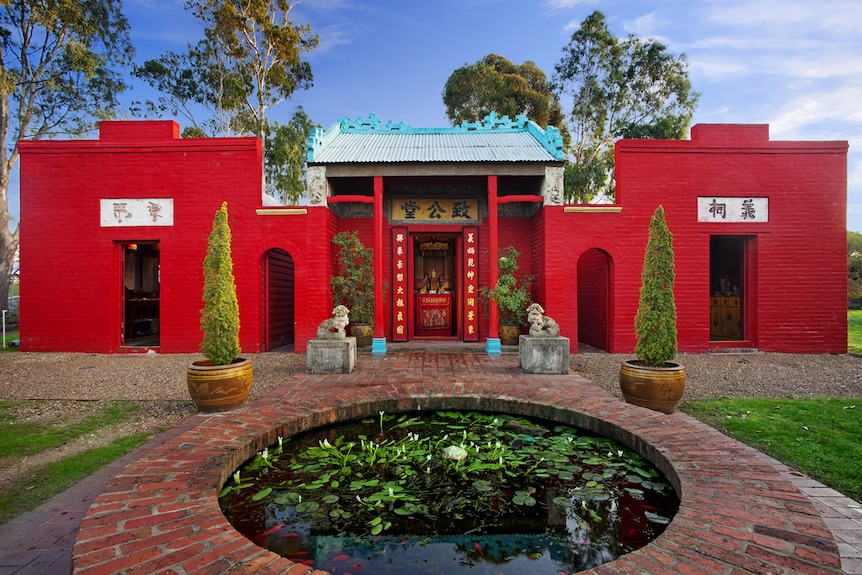 From a low angle, you look across a red brick water feature that shows Bendigo's bright read Joss House Temple.
