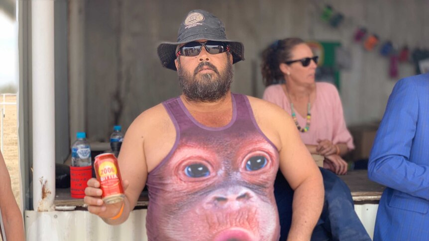 A man holds a can of drink and wearing a monkey singlet