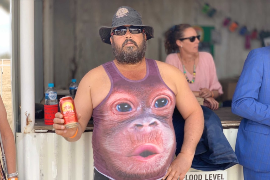 A man holds a can of drink and wearing a monkey singlet
