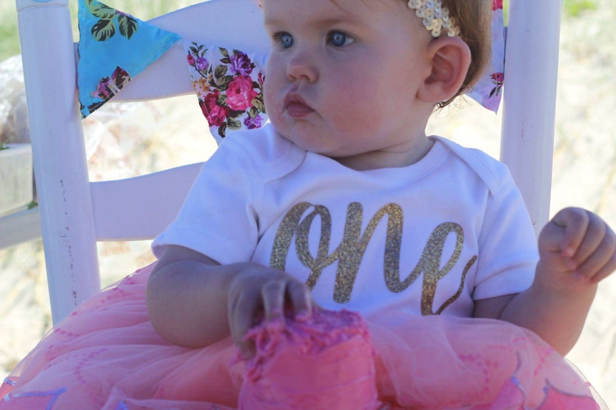 A cute baby on a chair with floral bunting behind it