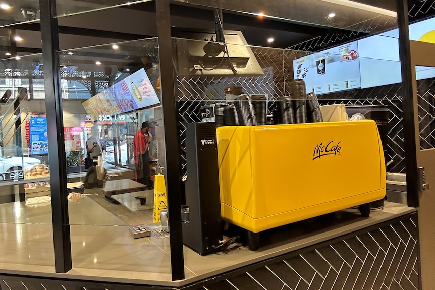 A McDonald's counter with a McCafe coffee machine and clear screens around it