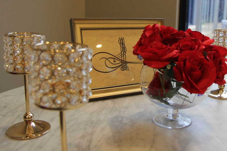 A small marble table holds a vase of roses and Islamic artwork.