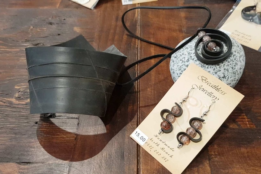 A black bit of tyre tube lays next to a pair of earrings made of tyre tubes.