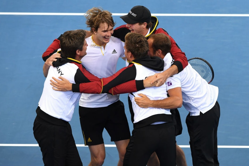 Alexander Zverev is surrounded by teammates as they celebrate on the court.