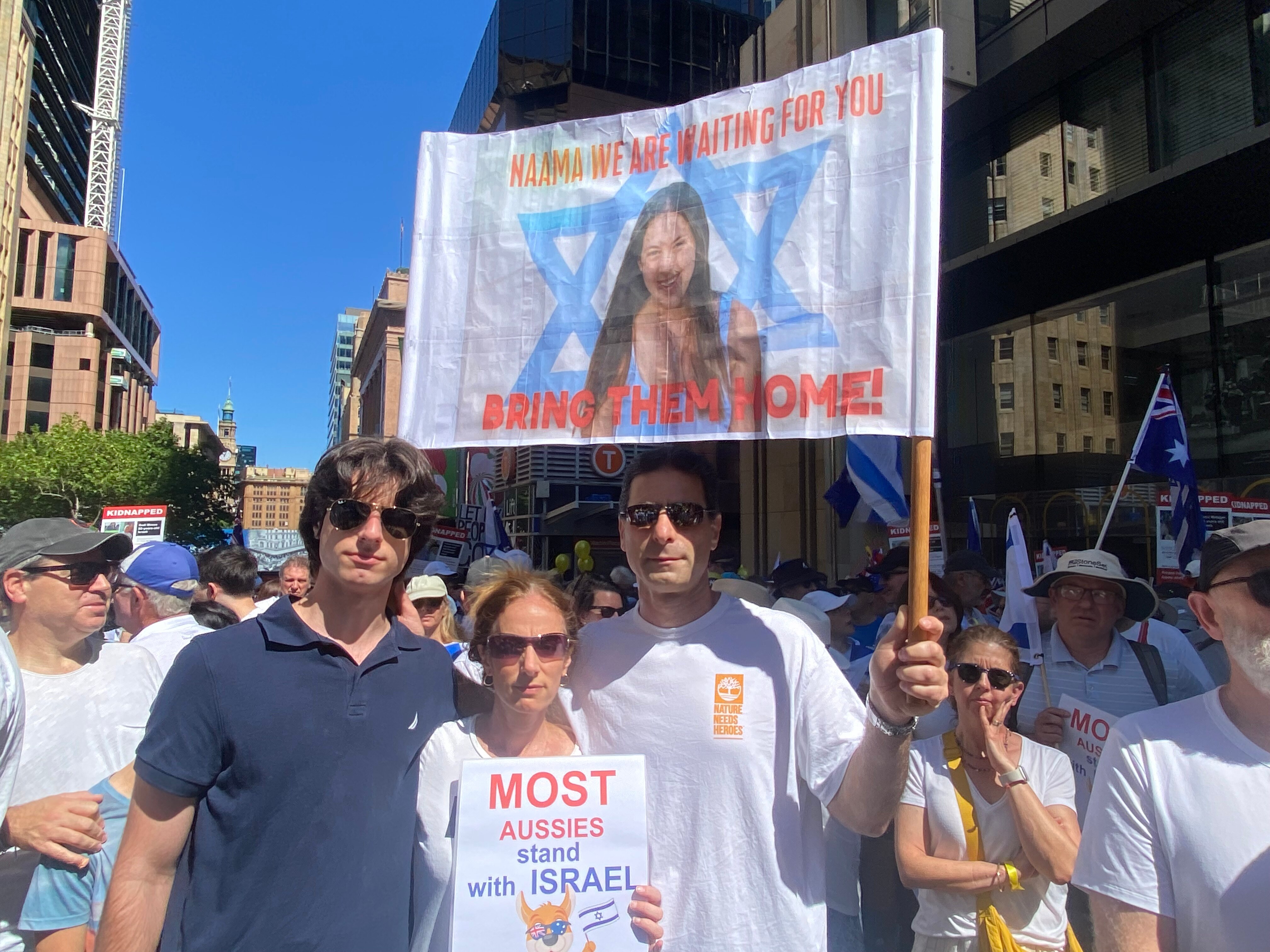 Two men and a woman stand together, holding a sign with Naama on it