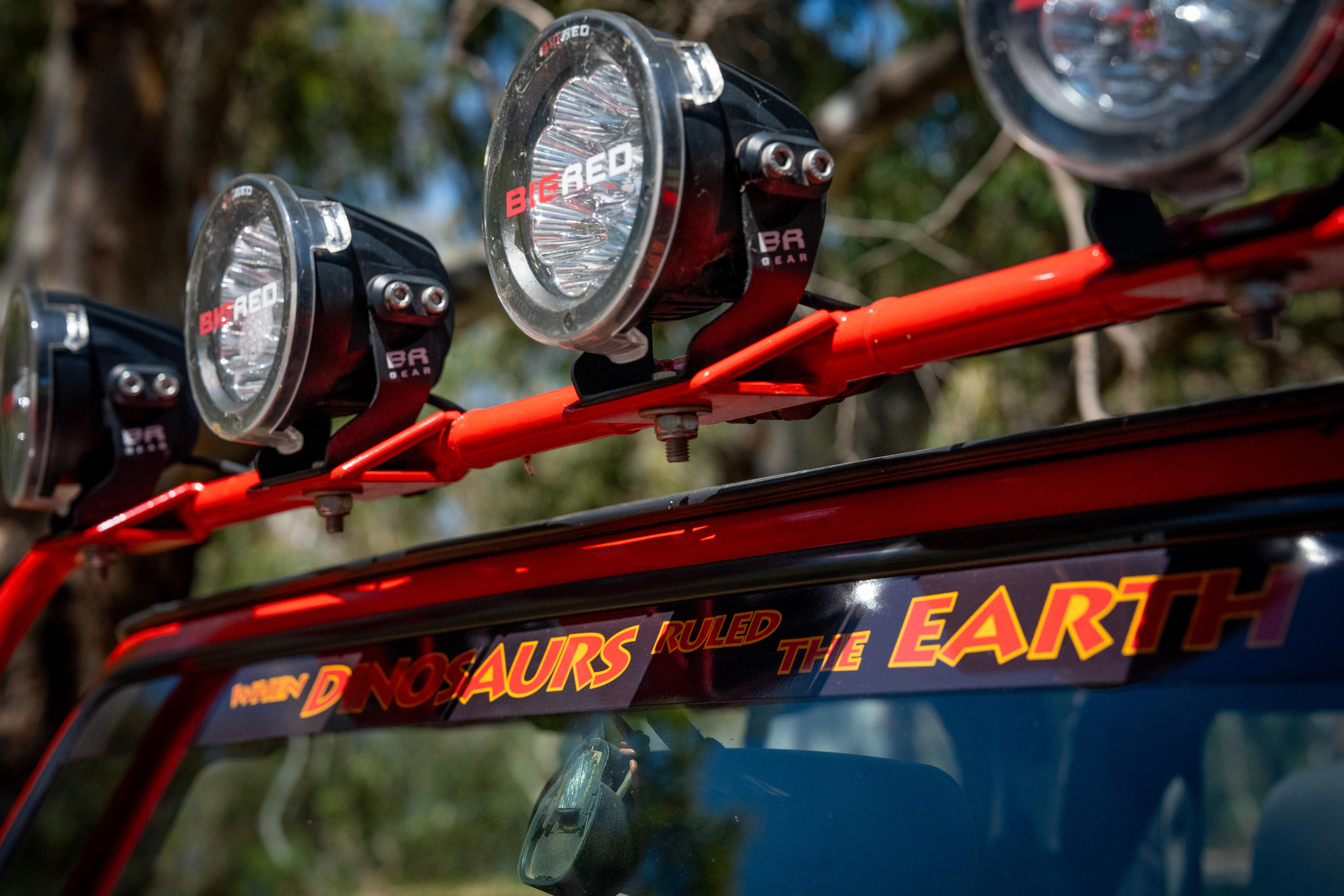 Grandes linternas montadas en el techo de un vehículo. Debajo de una pegatina puedes leer cuando los dinosaurios gobernaban la tierra.