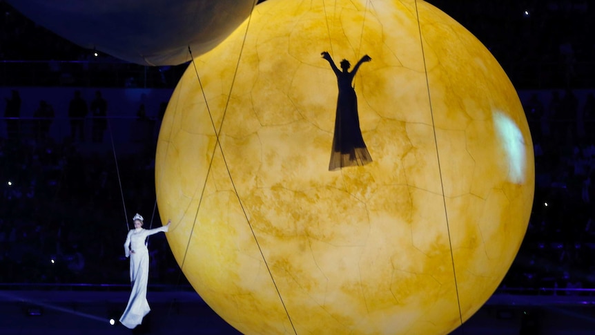 Performers on wires suspended with a golden moon