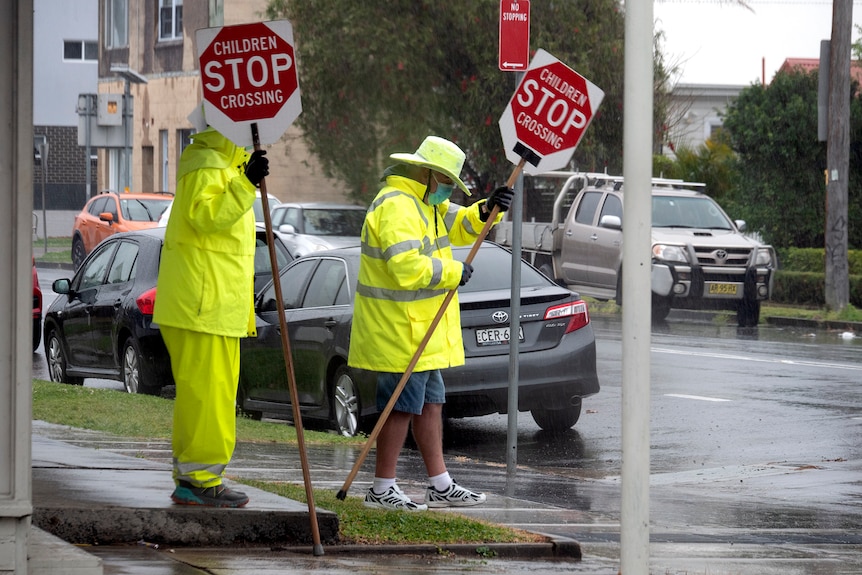Pedestrian crossing supervisors wearing face masks in the rain 