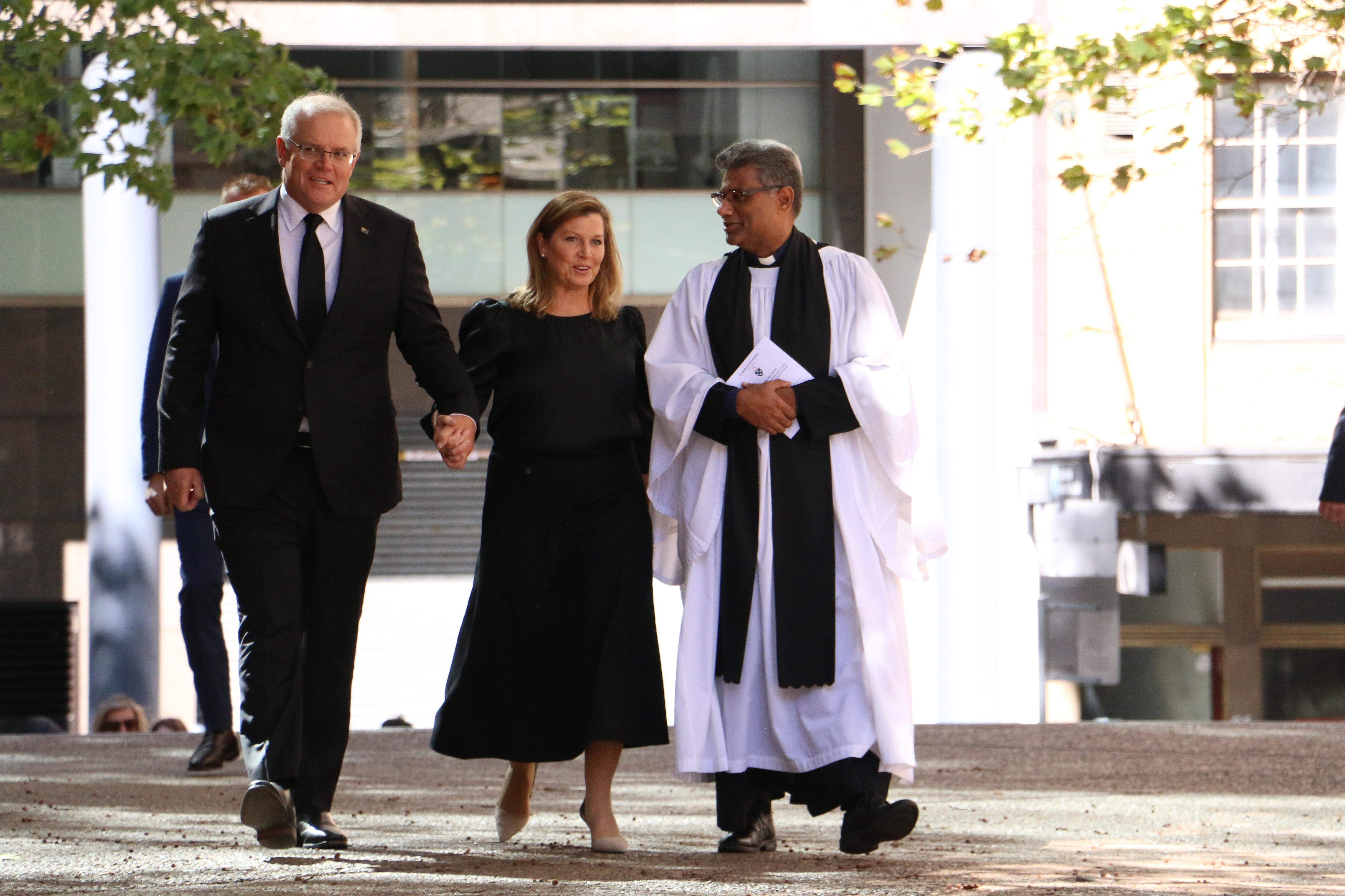The Prime Minister holds his wife's hand as they walk with a church minister.