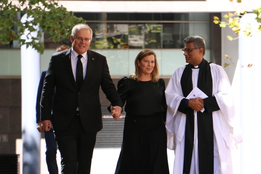 Le premier ministre tient la main de sa femme alors qu'ils marchent avec un pasteur de l'église.