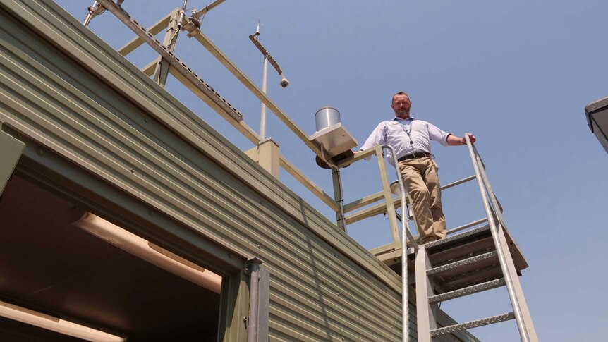 A man standing on top of a metal ladder on the side of an air pollution monitoring machine.