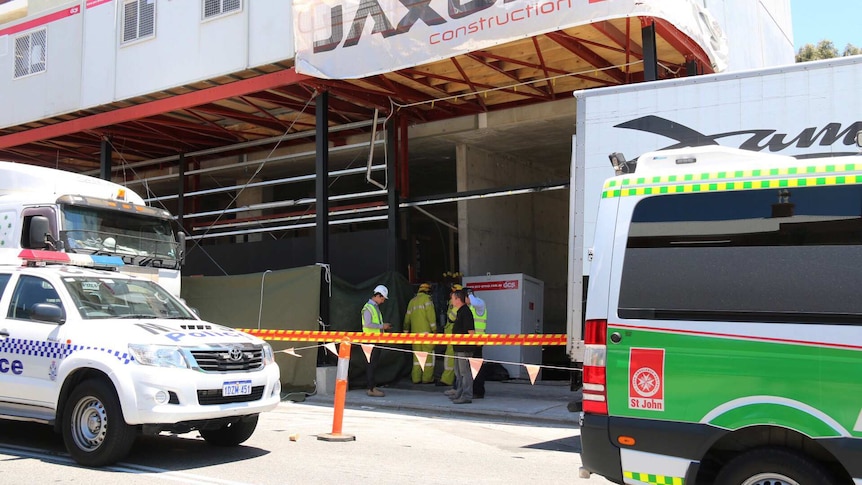 A police car and an ambulance sit parked outside a building site as workers stand at the entrance.