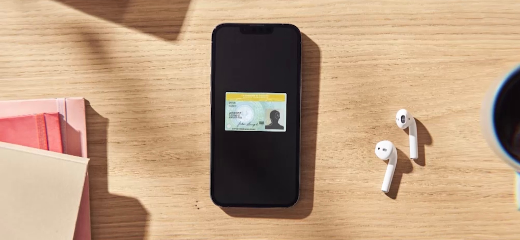 A blank mobile phone with a picture of a drivers licence lies on a wooden-style desk with ear buds.