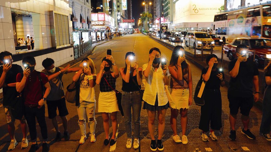A group of young protesters line up next to each other and hold up their phones