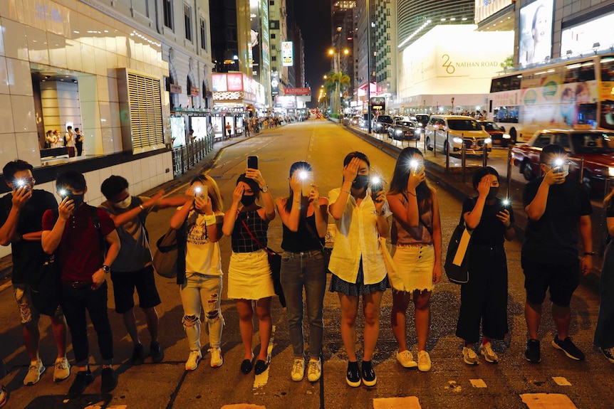 A group of young protesters line up next to each other and hold up their phones