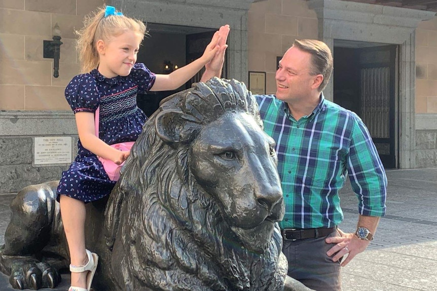 A girl sits on a lion statue outside town hall and hi-fives Adrian Schrinner