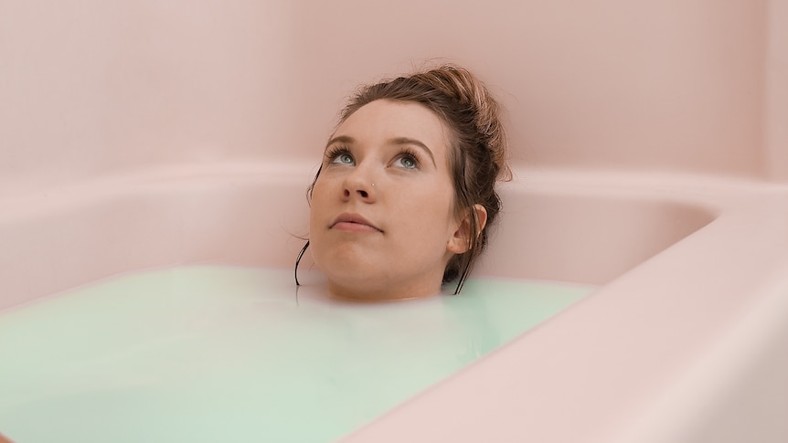 A young woman lying in a pink bath.