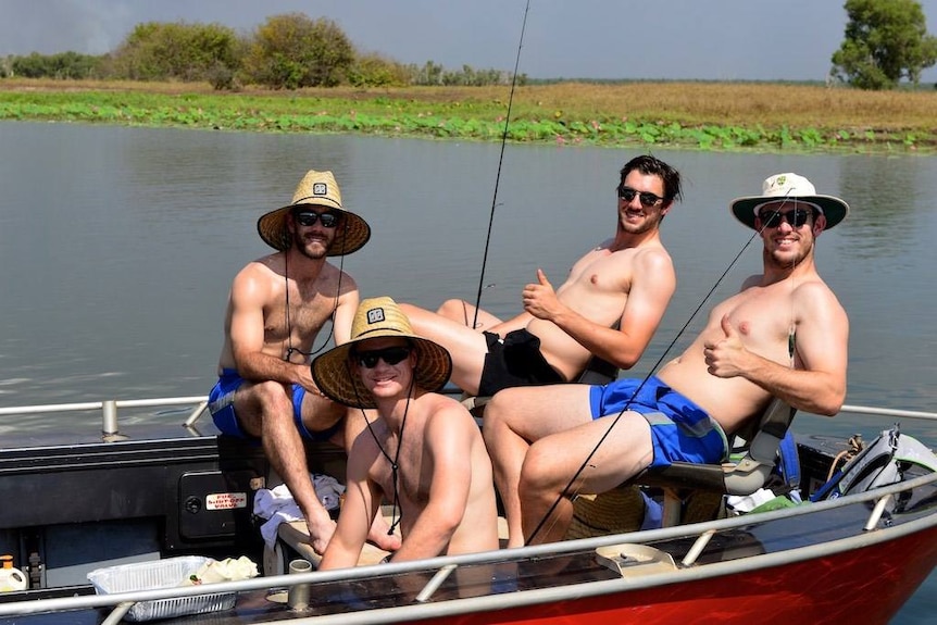 Four men sit in a tinny boat and smile for camera