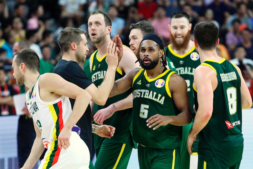 Patty Mills celebrates with boomers teammates, all wearing green singlets with gold trim with Australia in white letters