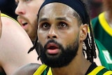 Patty Mills celebrates with boomers teammates, all wearing green singlets with gold trim with Australia in white letters