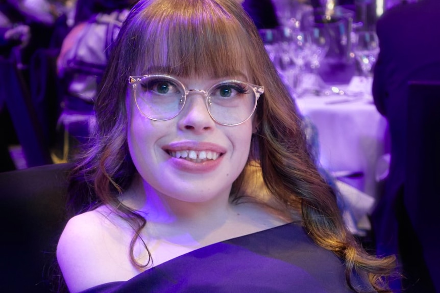 Ashleigh Gibson, who has long auburn hair and glasses, poses for a photo at a formal event