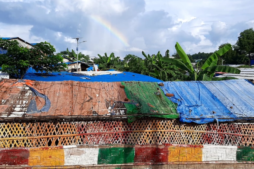 A brightly coloured makeshift building, with a rainbow in the background