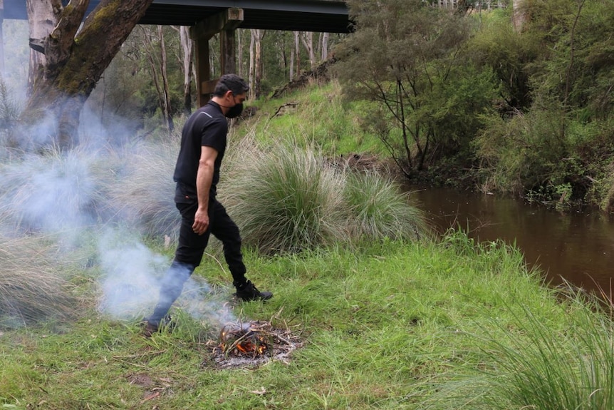 A man with a fire next to a river.