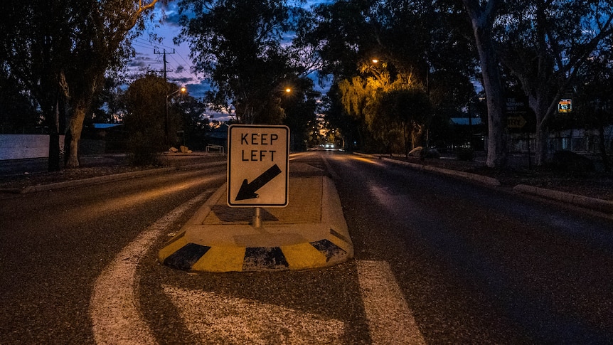 a dark street showing a median strip and keep left sign