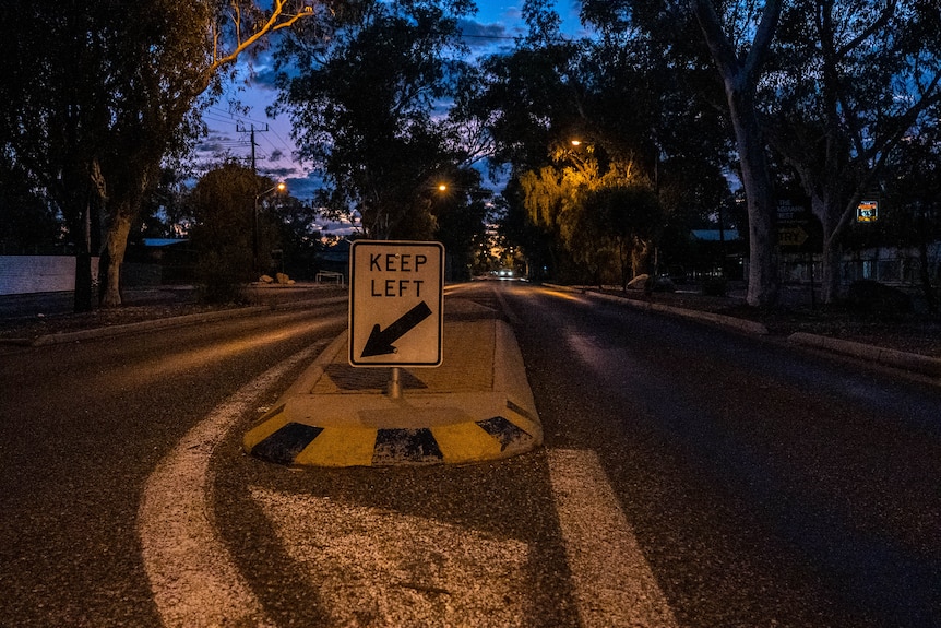 a dark street showing a median strip and keep left sign