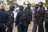 A group of police officers wear helmets, goggles, vests and balaclavas.