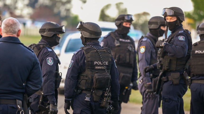 A group of police officers wear helmets, goggles, vests and balaclavas.