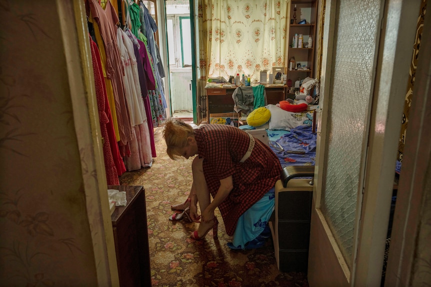 Medic volunteer Nataliia Voronkova is sitting in a bedroom, bent over her feet and strapping on her high heels. 