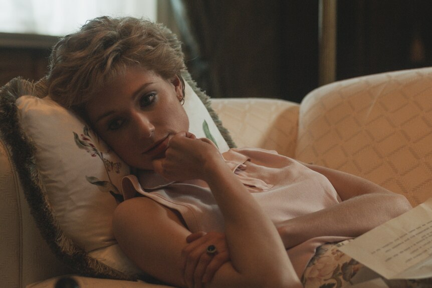 Diana lies on a chaise lounge and looks off into the distance with a letter open on her lap.