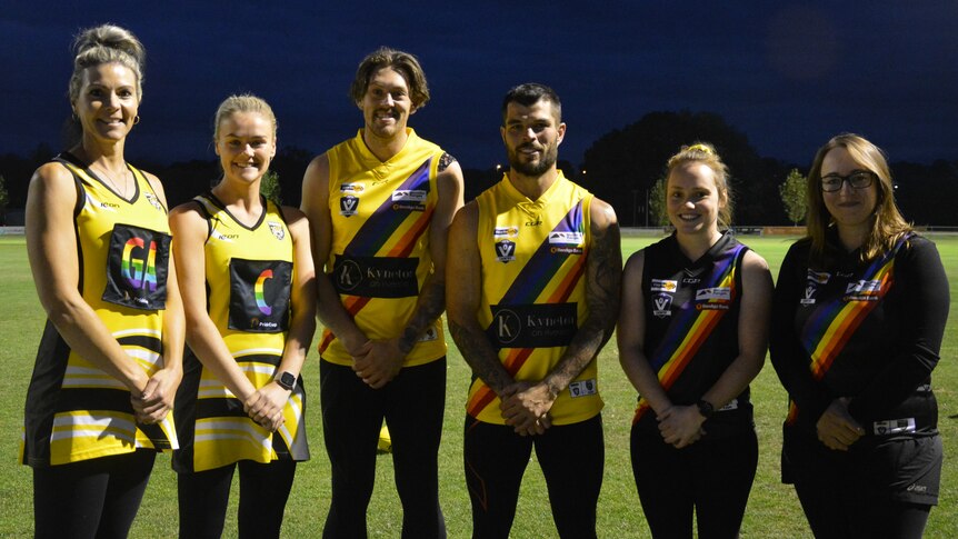A group of people face the camera wearing their football and netball guernseys