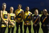 A group of people face the camera wearing their football and netball guernseys
